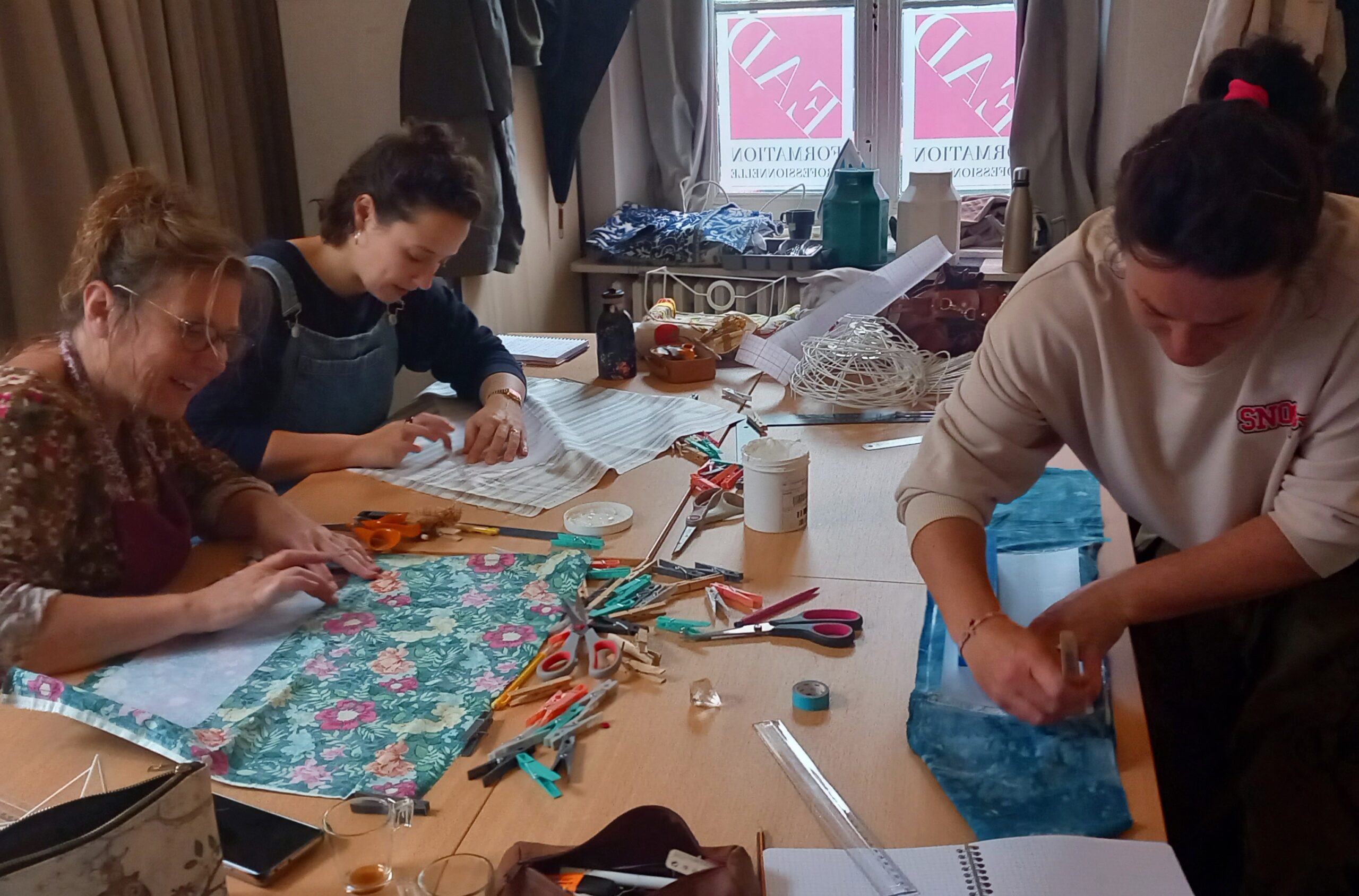 Groupe d’apprenantes travaillant sur leurs tissus et gabarits dans un atelier, illustrant l’apprentissage collaboratif du métier d’abat-jouriste.