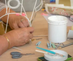 Mains d’un stagiaire concentré sur l’assemblage d’un abat-jour, symbole de l’apprentissage progressif du métier d’abat-jouriste.
