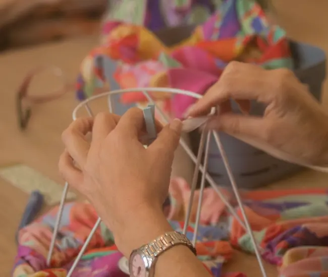 Mains fixant un ruban sur la structure métallique d’un abat-jour, illustrant le geste minutieux au cœur du métier d’abat-jouriste.