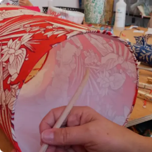 “Main ajustant l’intérieur d’un abat-jour tapissé d’un tissu rouge à motifs floraux, illustrant le soin apporté aux finitions.