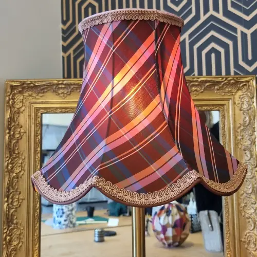 Abat-jour écossais aux courbes élégantes, illuminé de l’intérieur et souligné d’un galon décoratif.