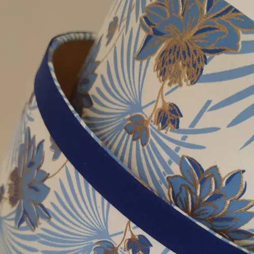 Détail d’un abat-jour contrecollé au tissu floral bleu et doré, soulignant l’importance du sens du détail dans cette technique.