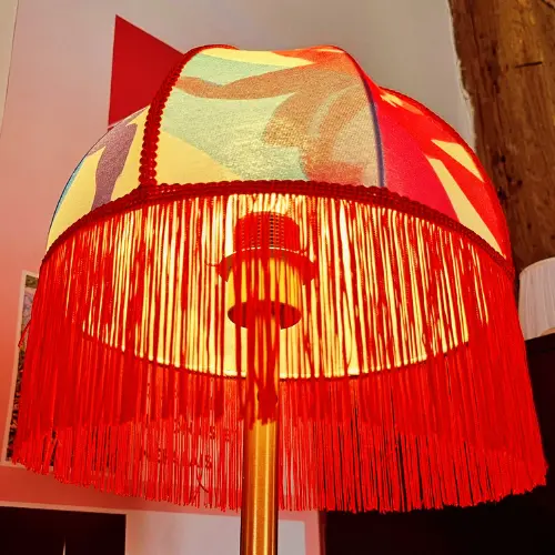 Abat-jour de style pagode habillé d’un tissu coloré et bordé de franges, illustrant la dimension créative et décorative du travail en tissu tendu.