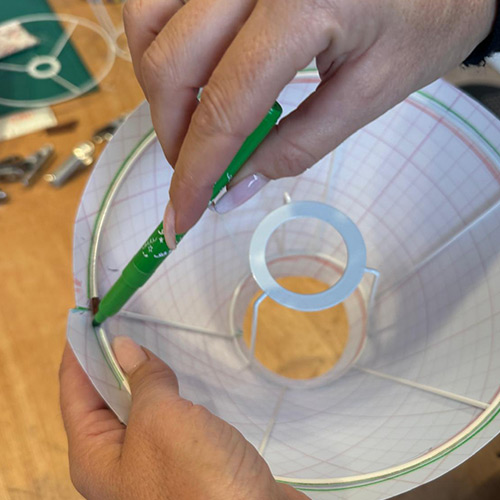 Main traçant un repère vert sur la structure d’un abat-jour pour préparer la pose des finitions.