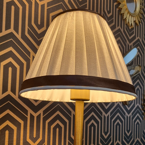 Abat-jour plissé en tissu beige texturé, bordé de galons foncés, présenté sur un pied doré.