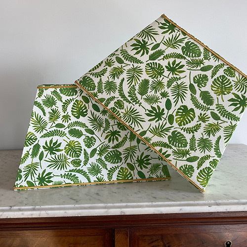 Deux abat-jour trapèze recouverts d’un tissu à feuilles tropicales vertes, posés sur un plateau en marbre.